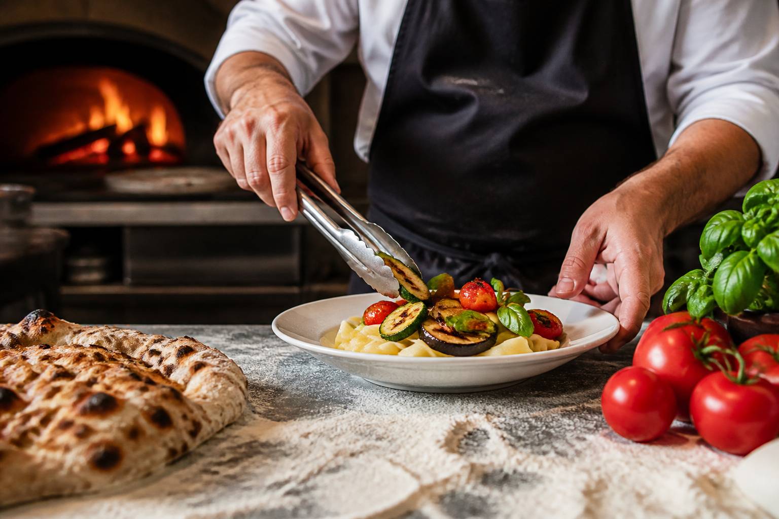 Mains de cuisinier dressant un plat de pâtes avec des légumes