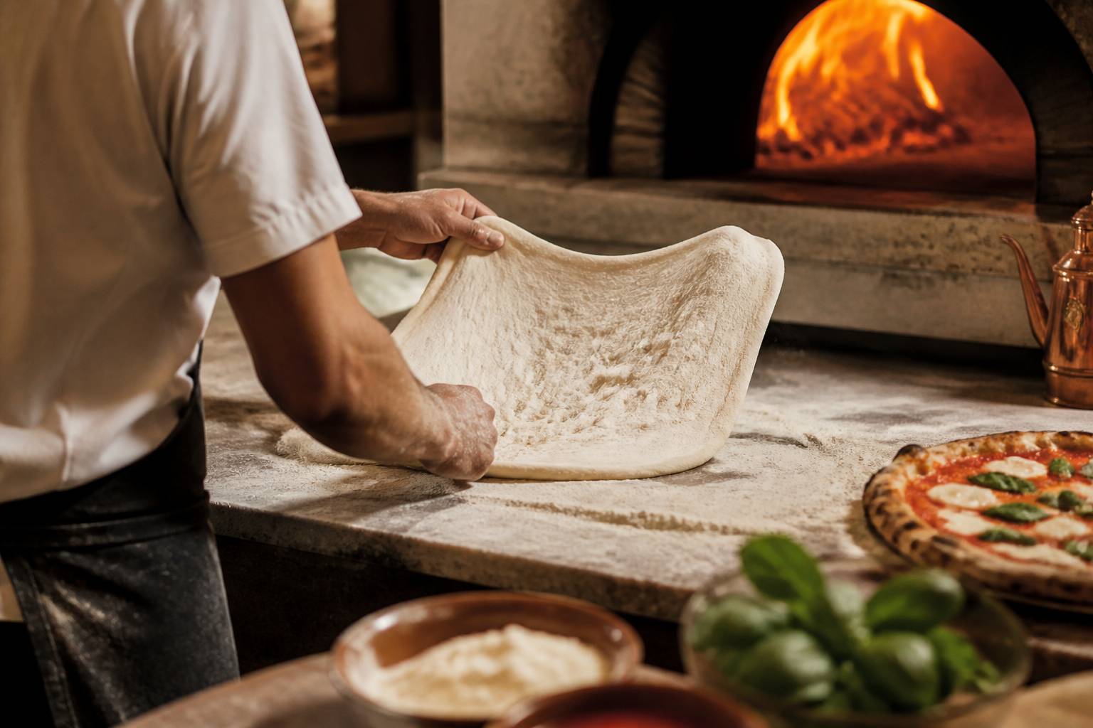 Pizzaiolo étirant une pâte alvéolée sur un plan de travail fariné près du four à bois